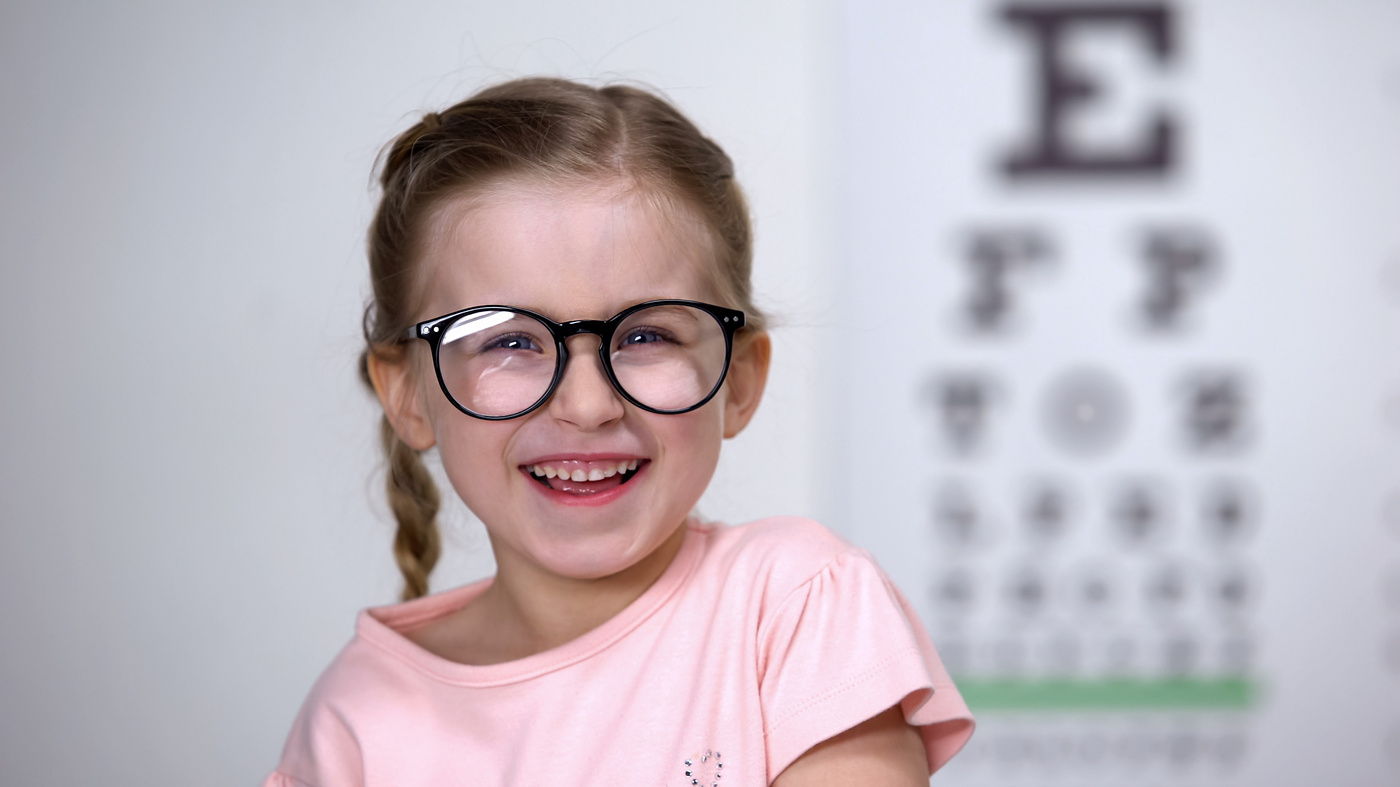 Fille qui rit, avec lunettes, devant planche d'acuité visuelle